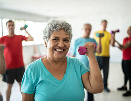 A woman in an exercise class smiles as she lifts a small hand weight.